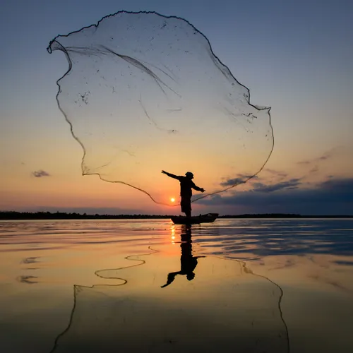 Fisherman casting a net in silhouette against an evening sky